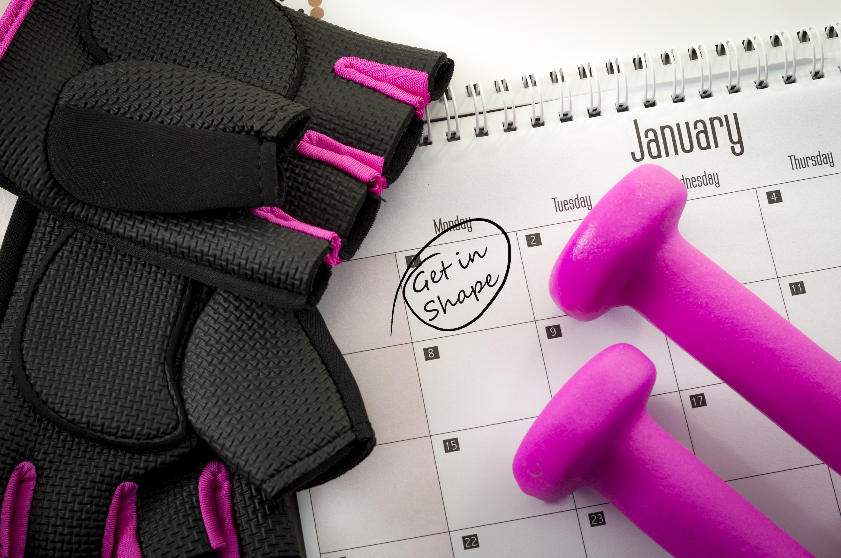 New year resolution and the desire to get in shape concept with a calendar with january first circled, gym equipment like purple dumbbells and pink and black workout gloves