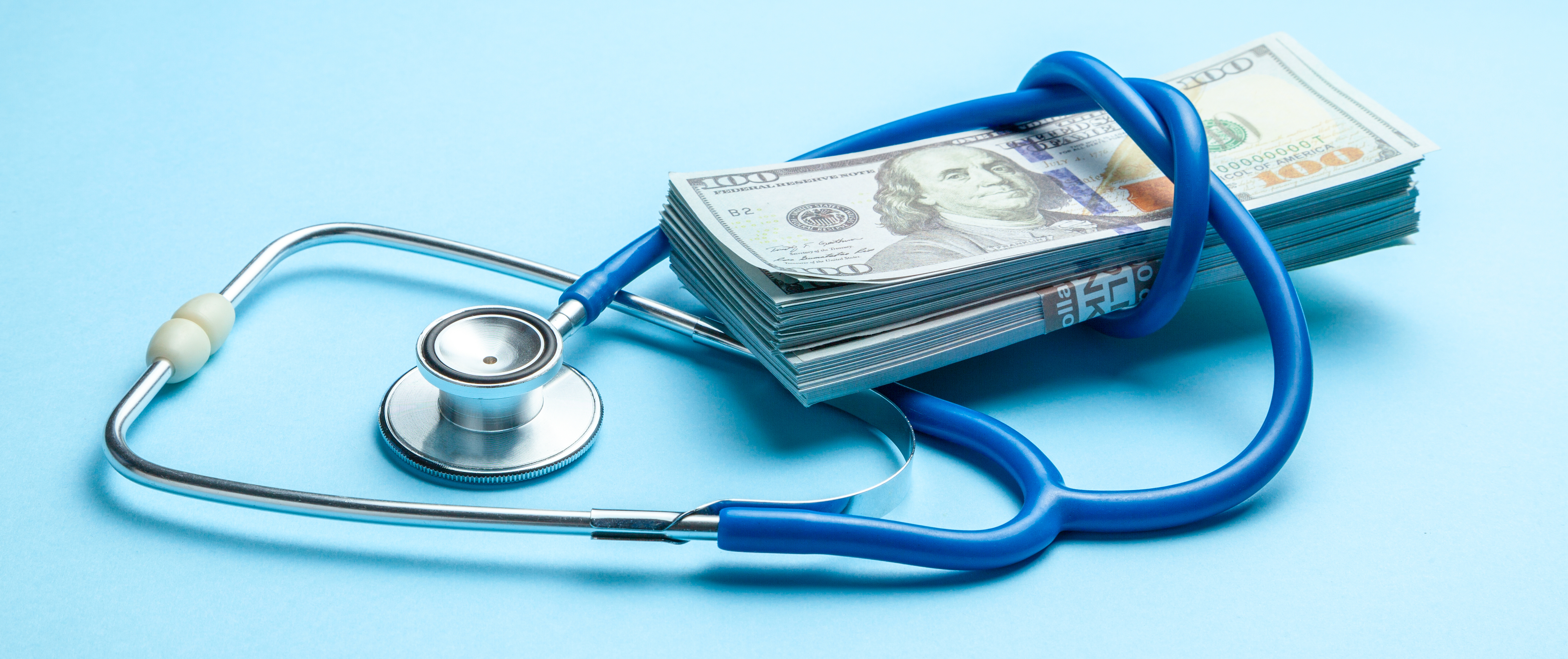 Stack of cash dollars and stethoscope on blue background. 