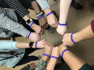 Creative Services staff members putting hands together in a circle with purple bracelets